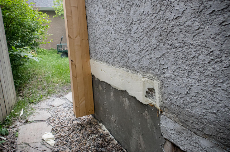 “Damaged exterior stucco wall with fresh patching near the base of a home during a stucco service in Henderson, NV”