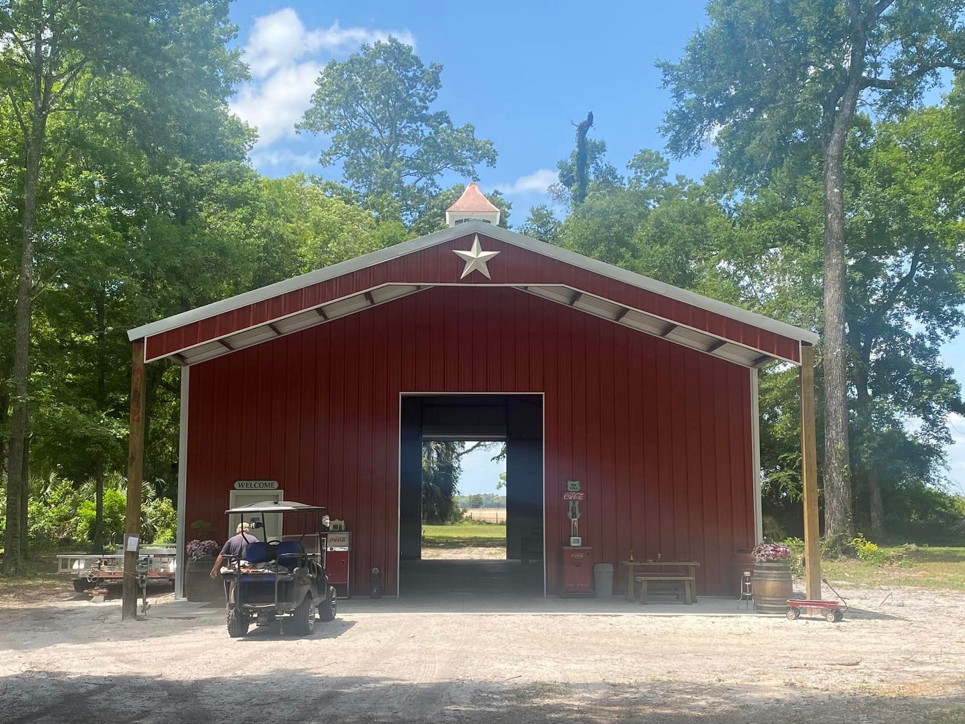 Red barn with open doorway and white star, surrounded by trees under a bright sky.
