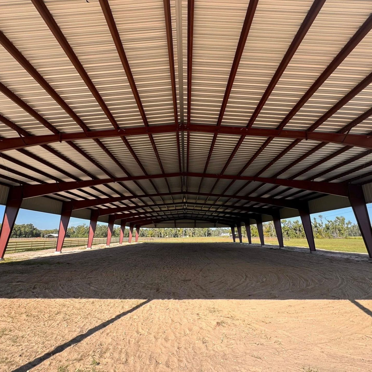 Open-sided metal pavilion with a corrugated roof over a dirt ground in a sunny field