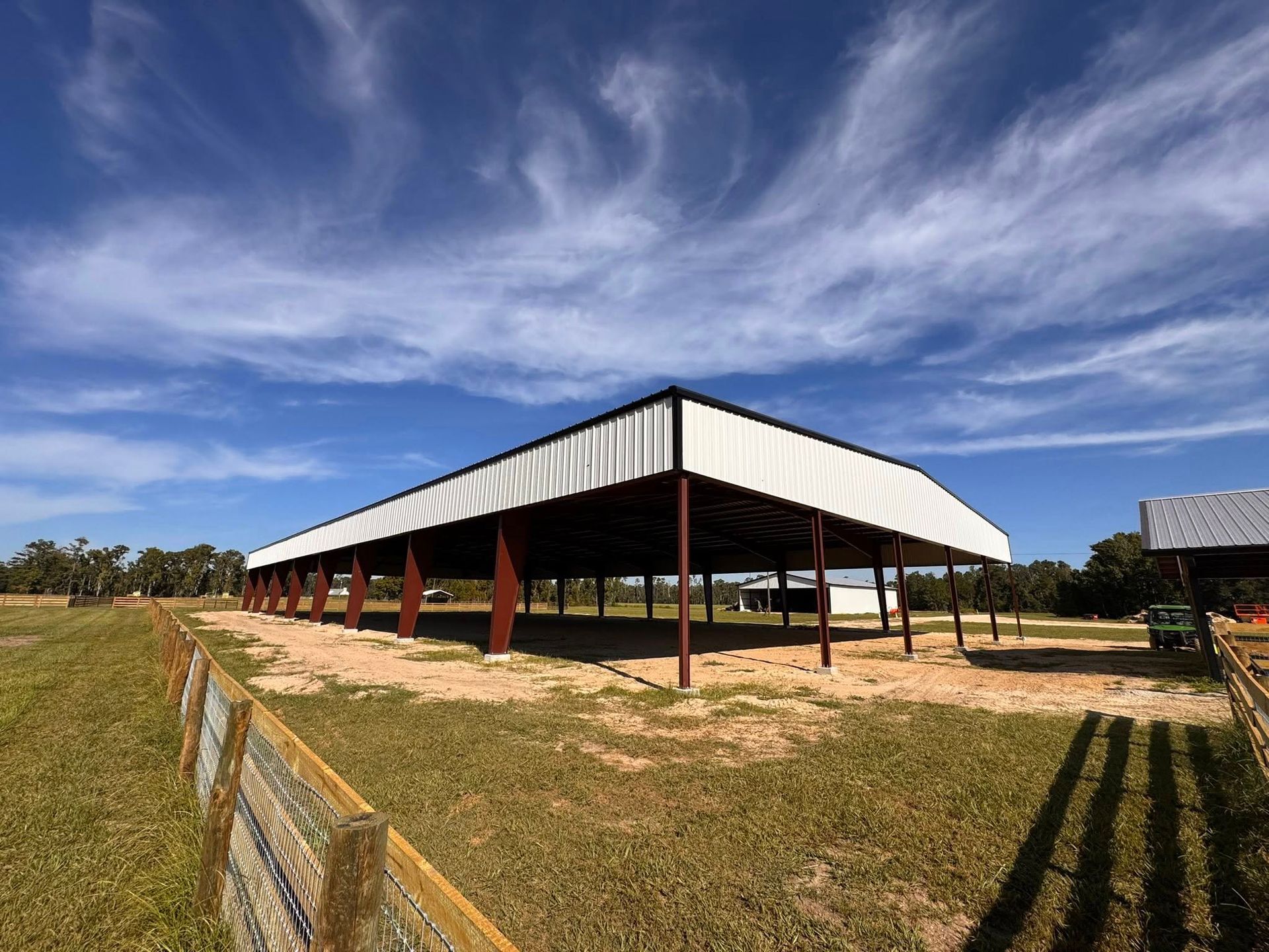 Open-sided barn with white roof and red posts in a dry field under a blue sky