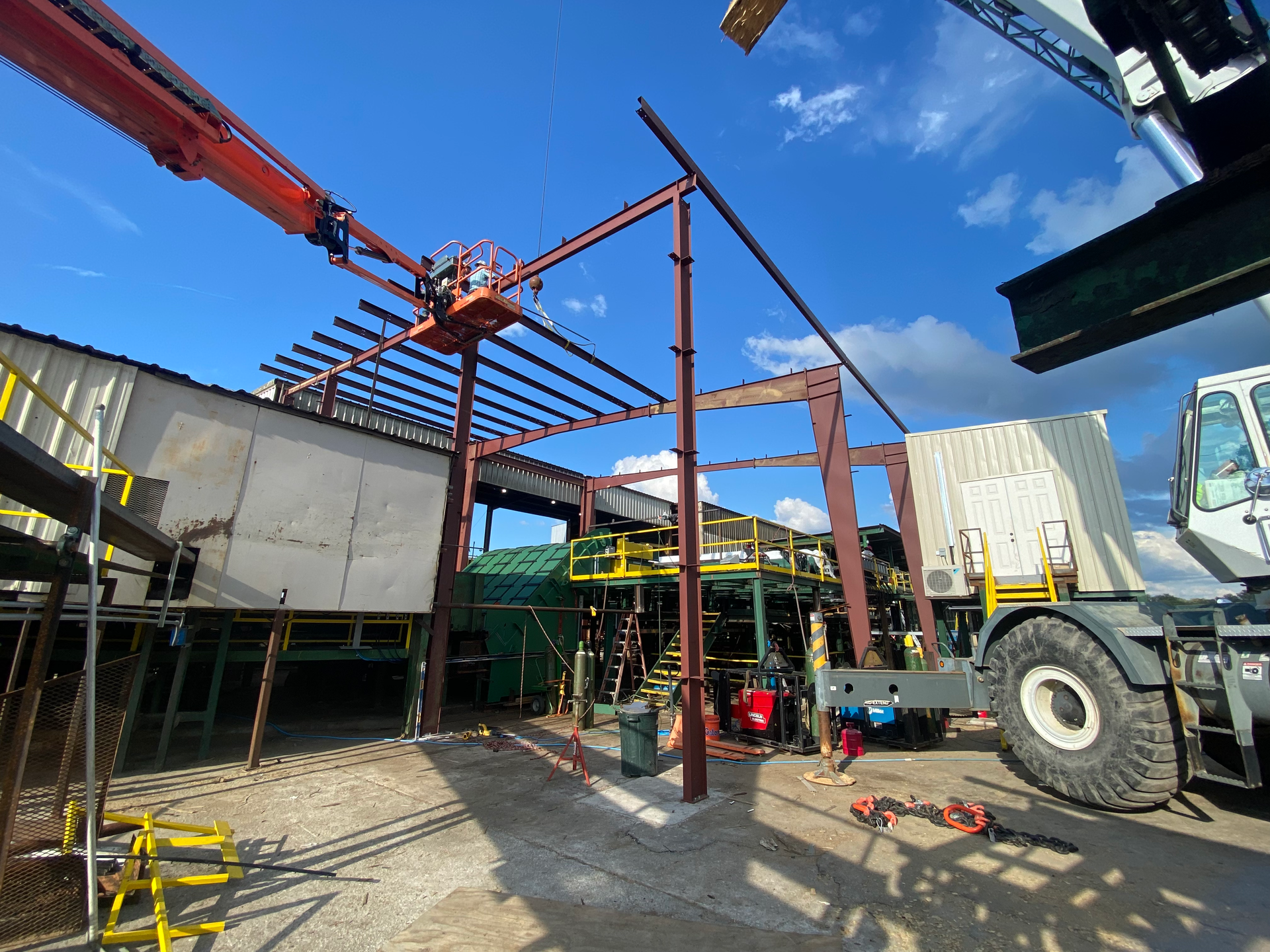 Construction site with steel frame, orange crane arm, and workers among scaffolding and equipment