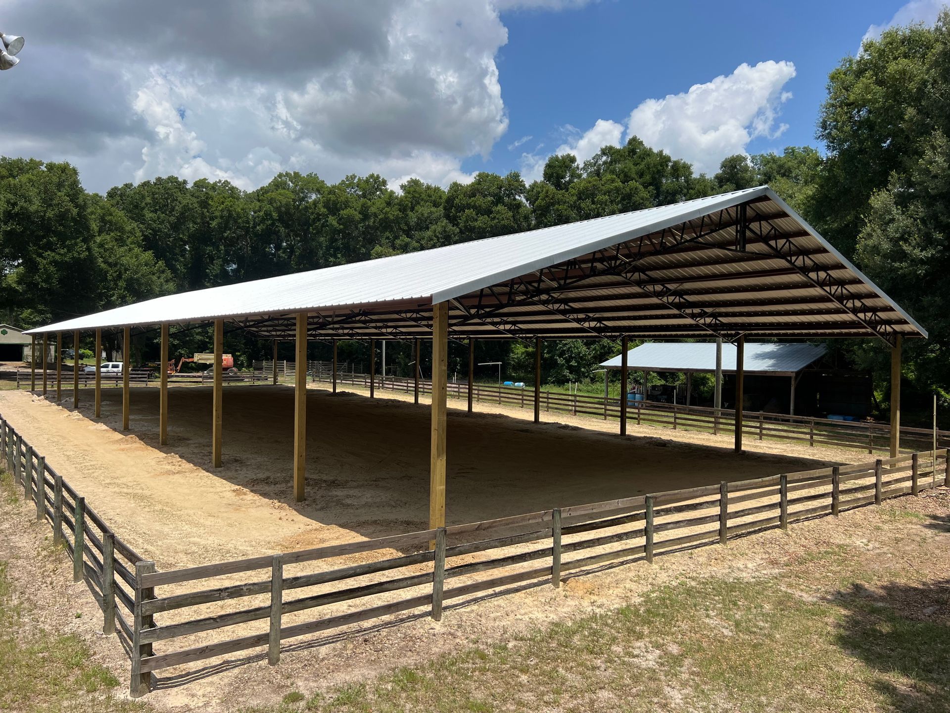 Covered outdoor livestock arena with a white metal roof and wooden fencing on a sunny day