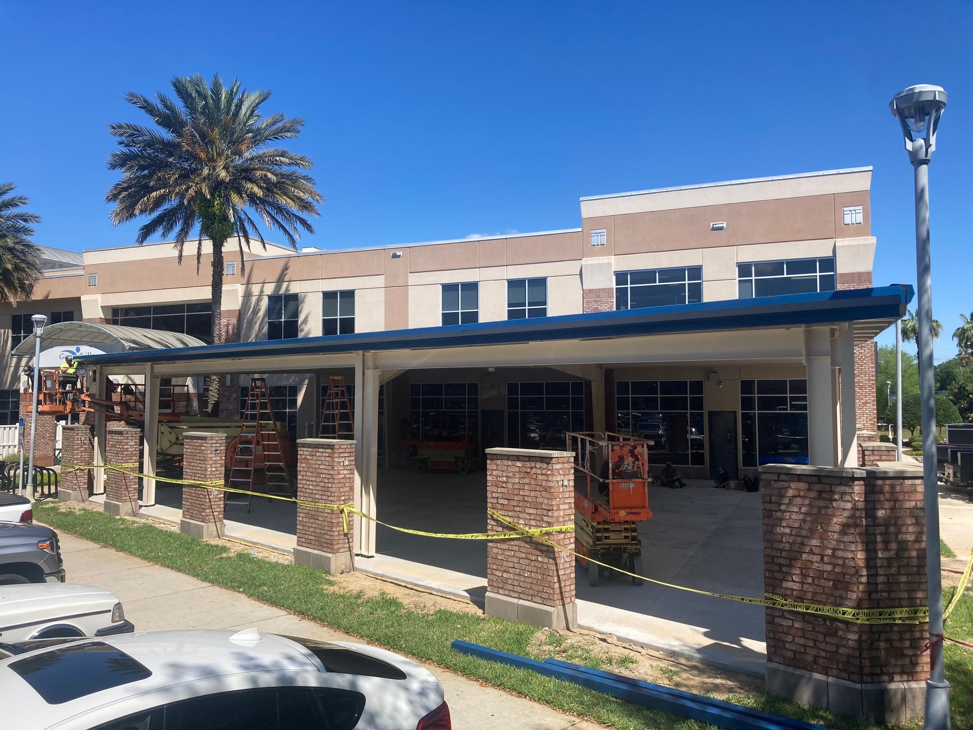 Historic building with covered walkway, brick columns, palm tree, and parked cars under a blue sky