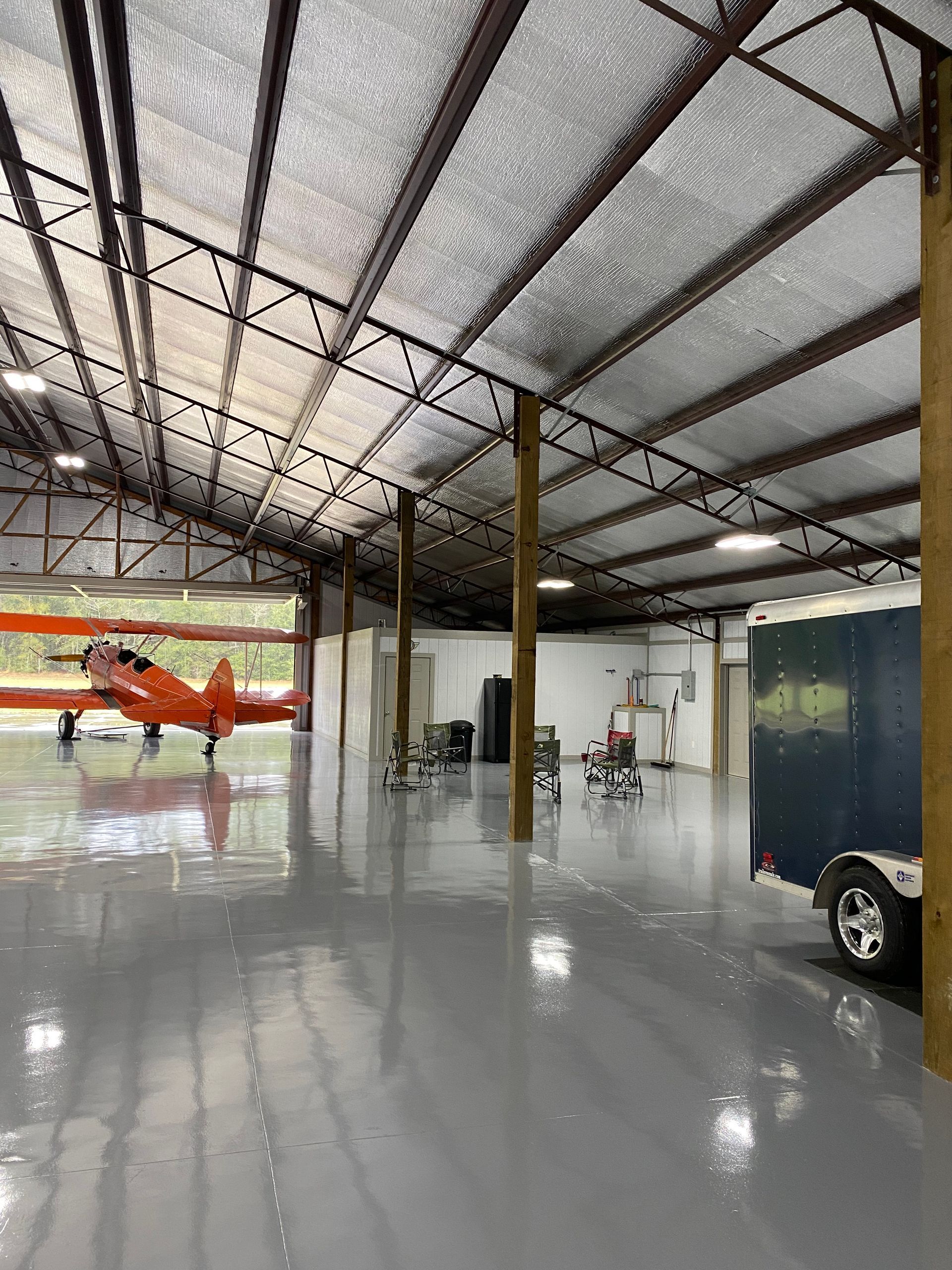 Hangar interior with a small orange plane, shiny floor, and a vehicle at the right edge