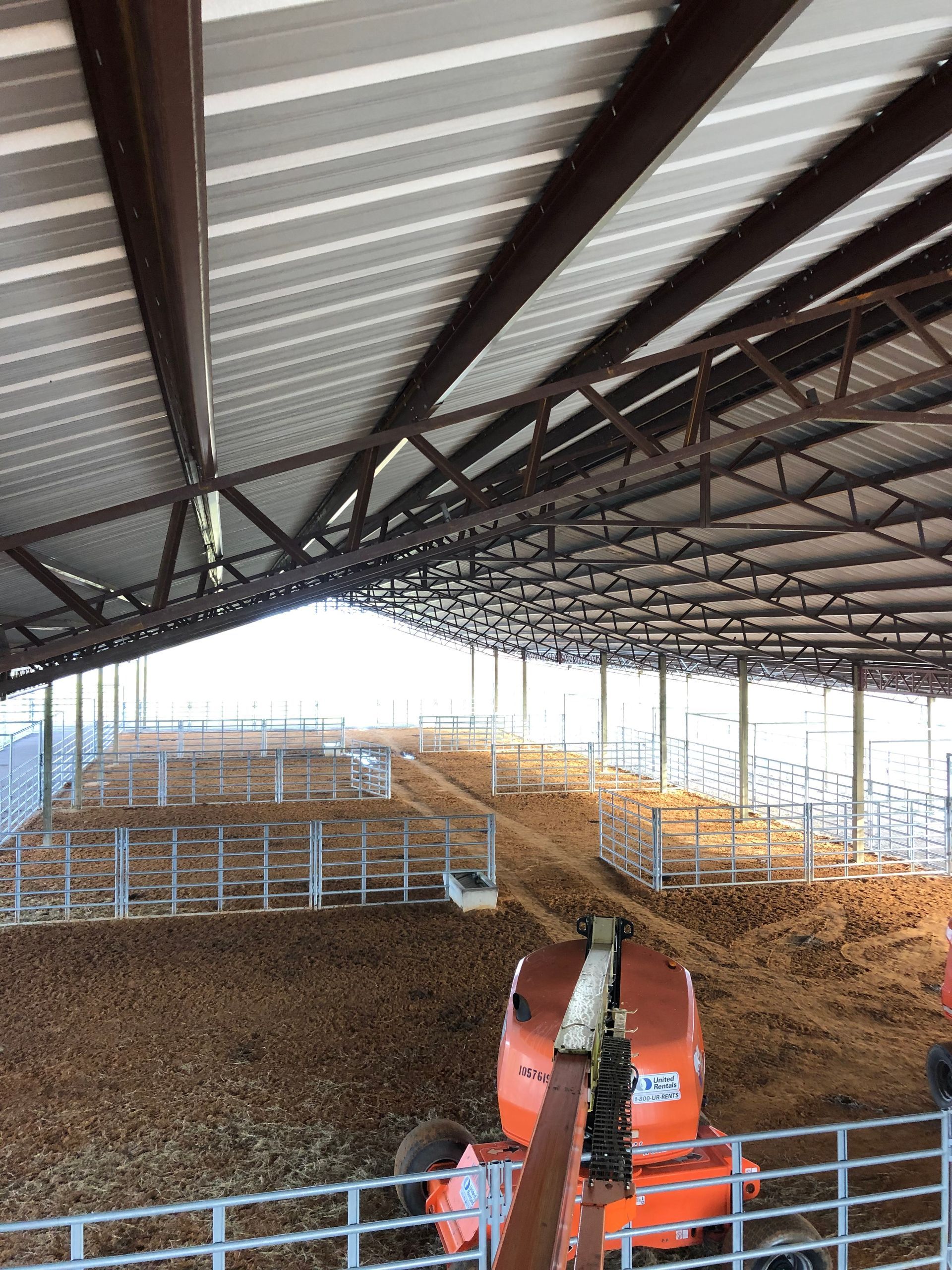 Interior of a cattle barn with pens, straw bedding, and a red tractor under a metal roof