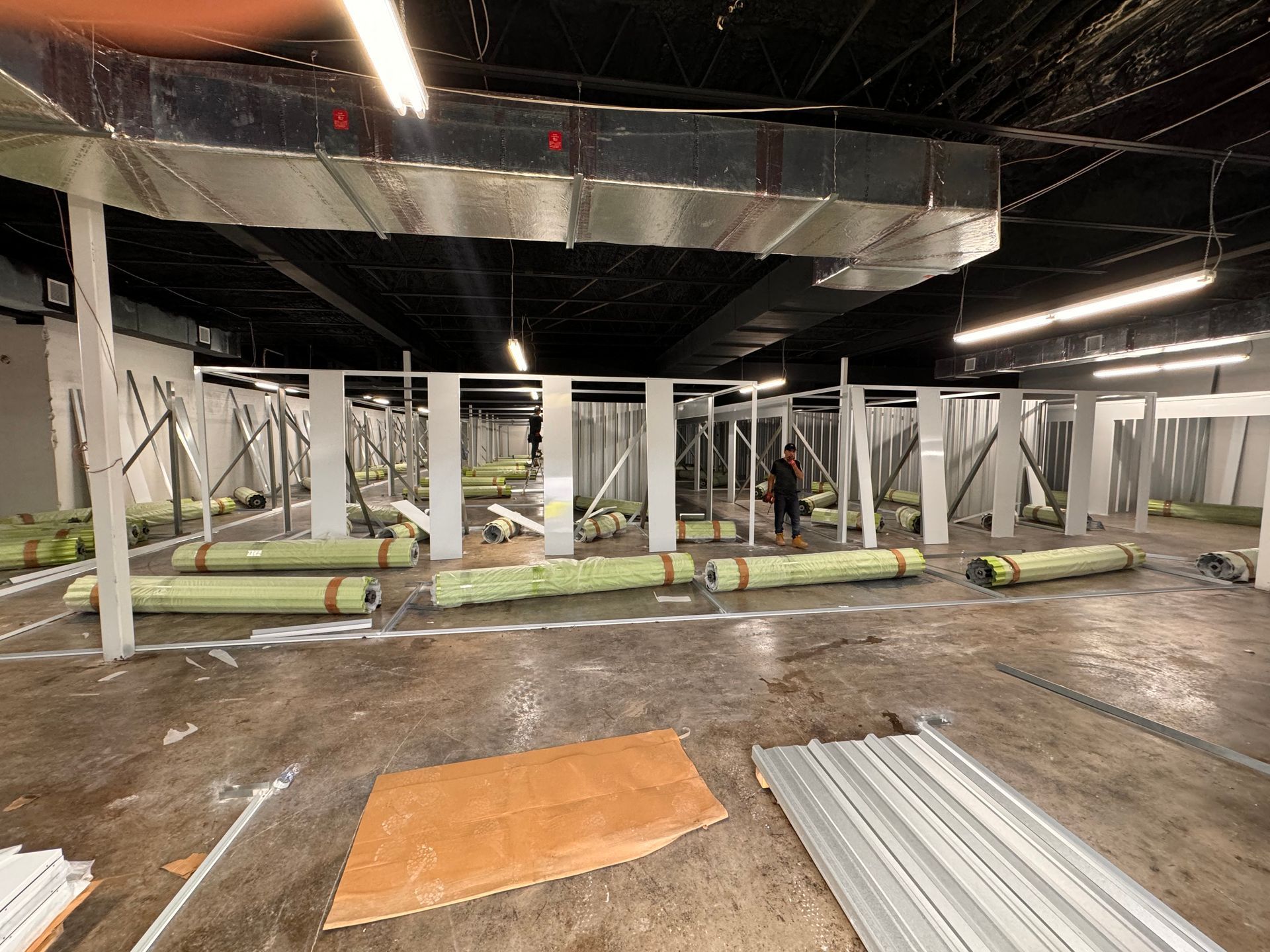 Damaged indoor space with collapsed ceiling panels, fallen pipes, and debris scattered across the floor