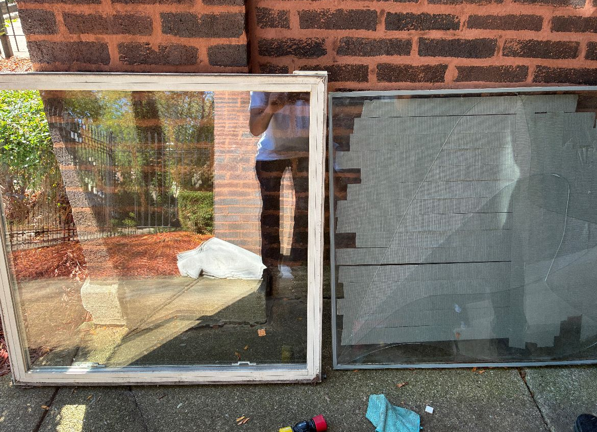 Two window screens leaning against a brick wall, with reflections in the left pane and a white bag on the ground.