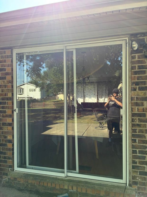 Sliding glass patio door on a brick house, reflecting a person holding a camera in the yard.