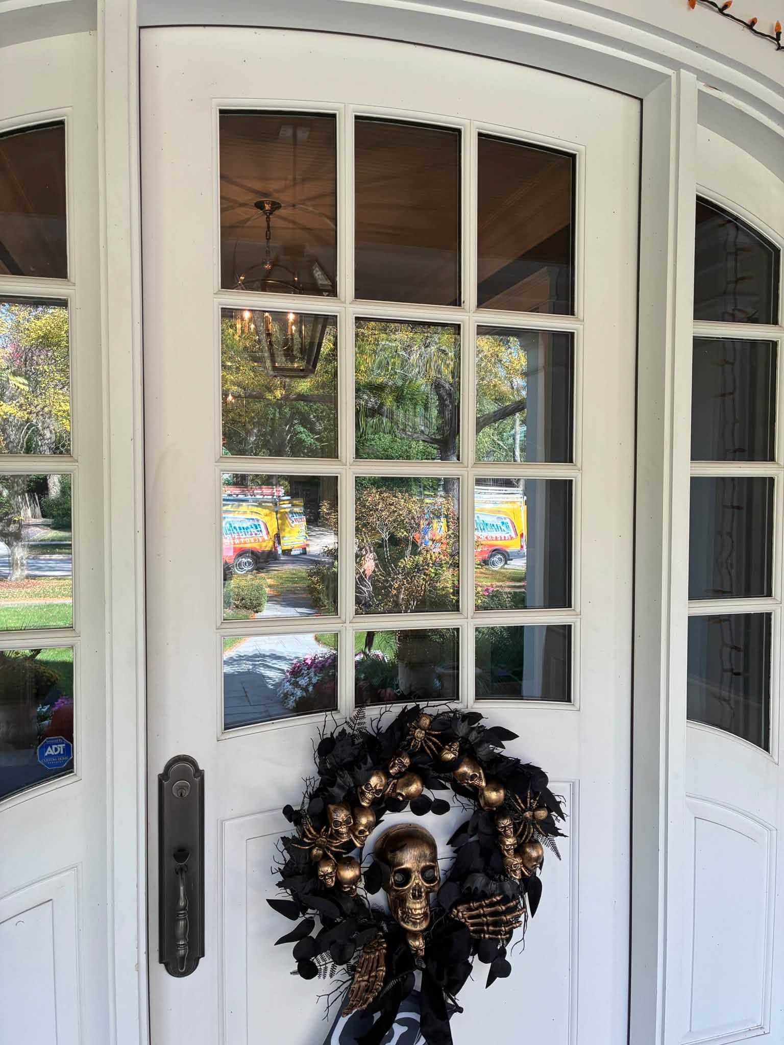 White front door with glass panes and a black-and-orange skull wreath hanging on it.