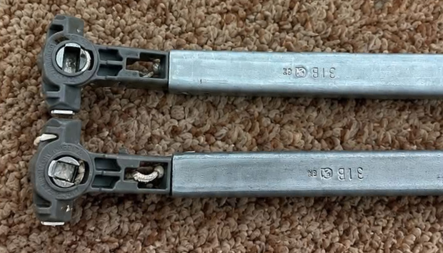 Two silver metal hinge arms on brown carpet, each with circular mounting end and locking mechanism.