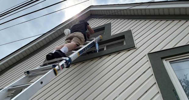 Person on a ladder fixing a roof window on a house siding exterior