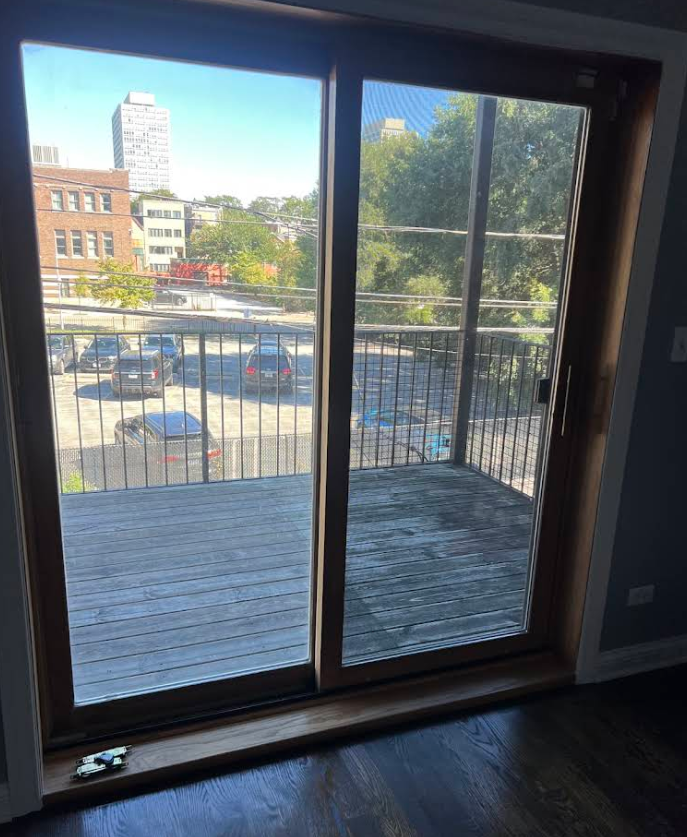 Sliding glass door opening to a balcony with a city street and trees outside