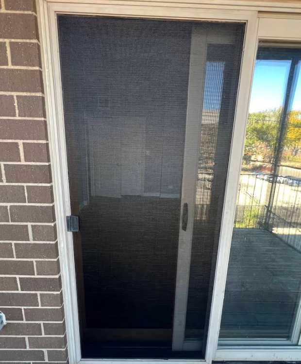 Closed dark screen door beside a glass sliding door on a brick patio.