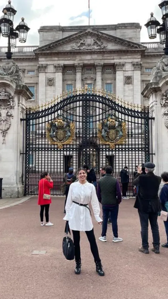 Tourists standing before ornate black-and-gold palace gates under a gray sky