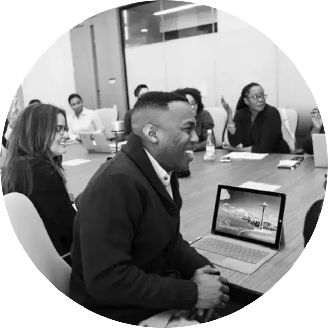 Meeting room with people seated around a conference table, one person using a laptop