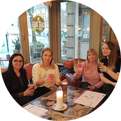 Four people seated at a café table, holding drinks and smiling near a candlelit table