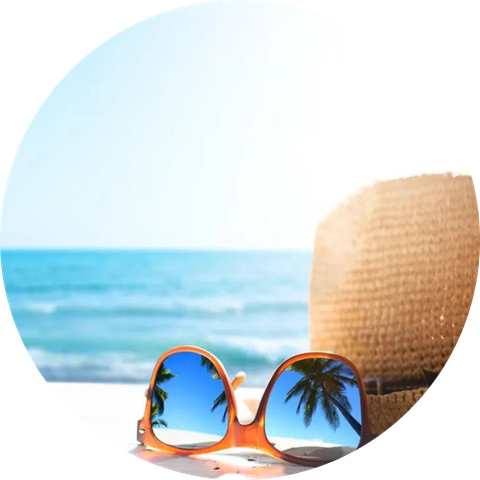 Orange sunglasses and a straw hat on a beach, with palm trees reflected in the lenses