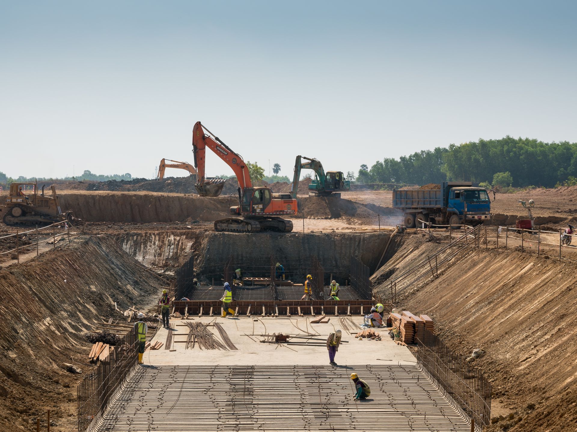 Construction site with excavators and workers in a deep concrete foundation trench