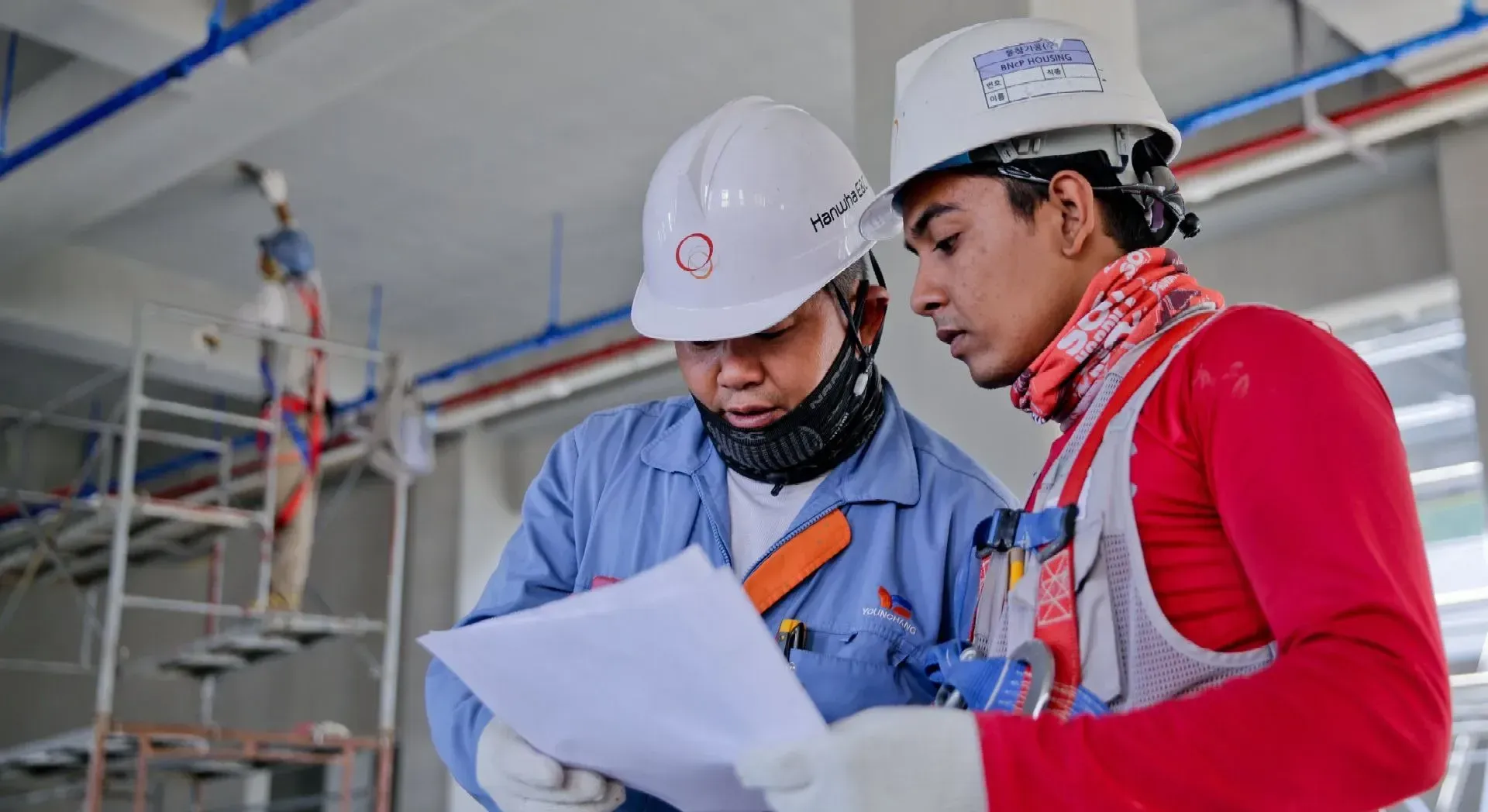 Two construction workers in hard hats reviewing blueprints at a building site