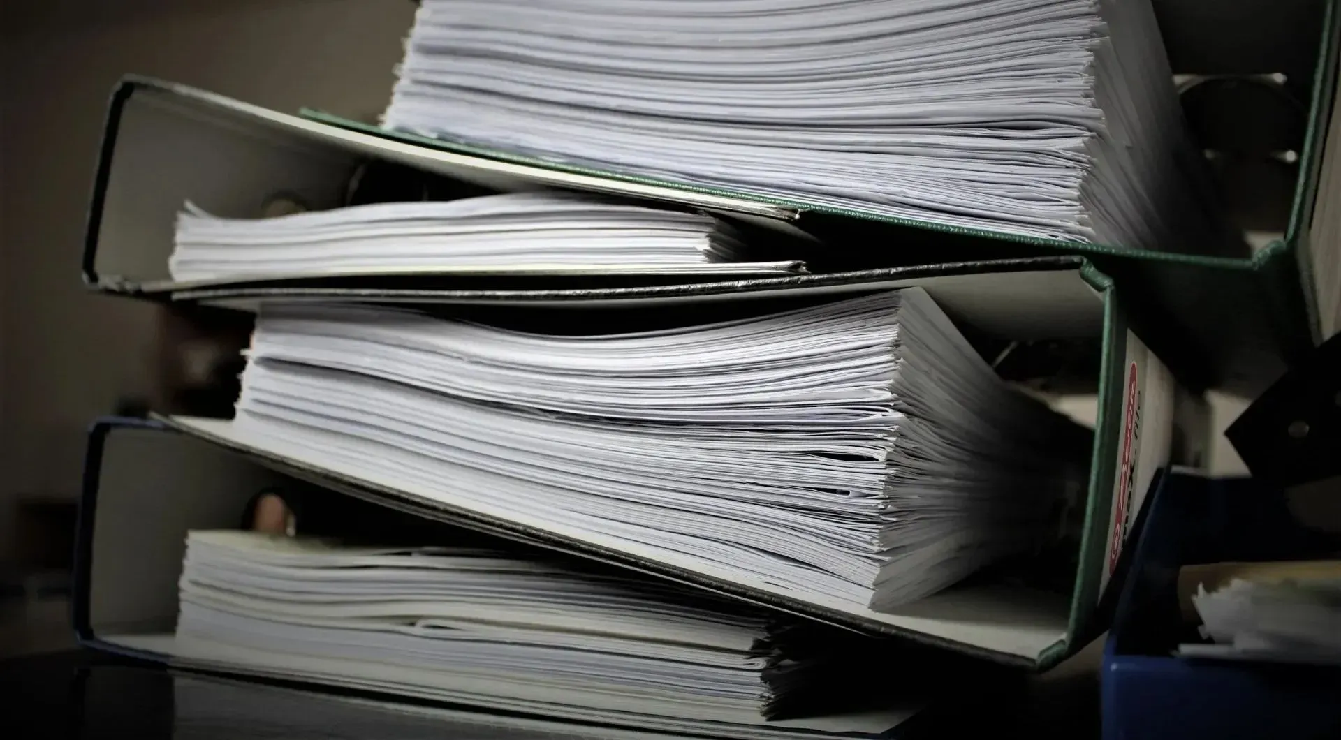 Stacked overflowing file folders filled with loose papers on a desk