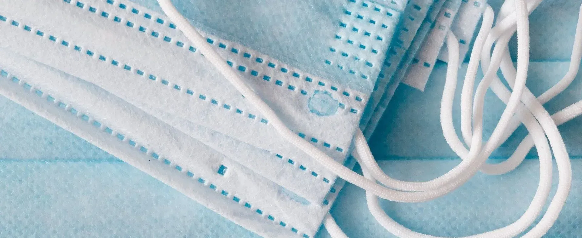 Blue disposable face masks with white elastic ear loops stacked together