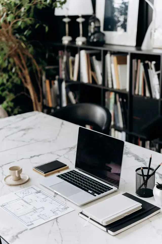 Modern office desk with open laptop, notebooks, coffee cup, and shelves in the background