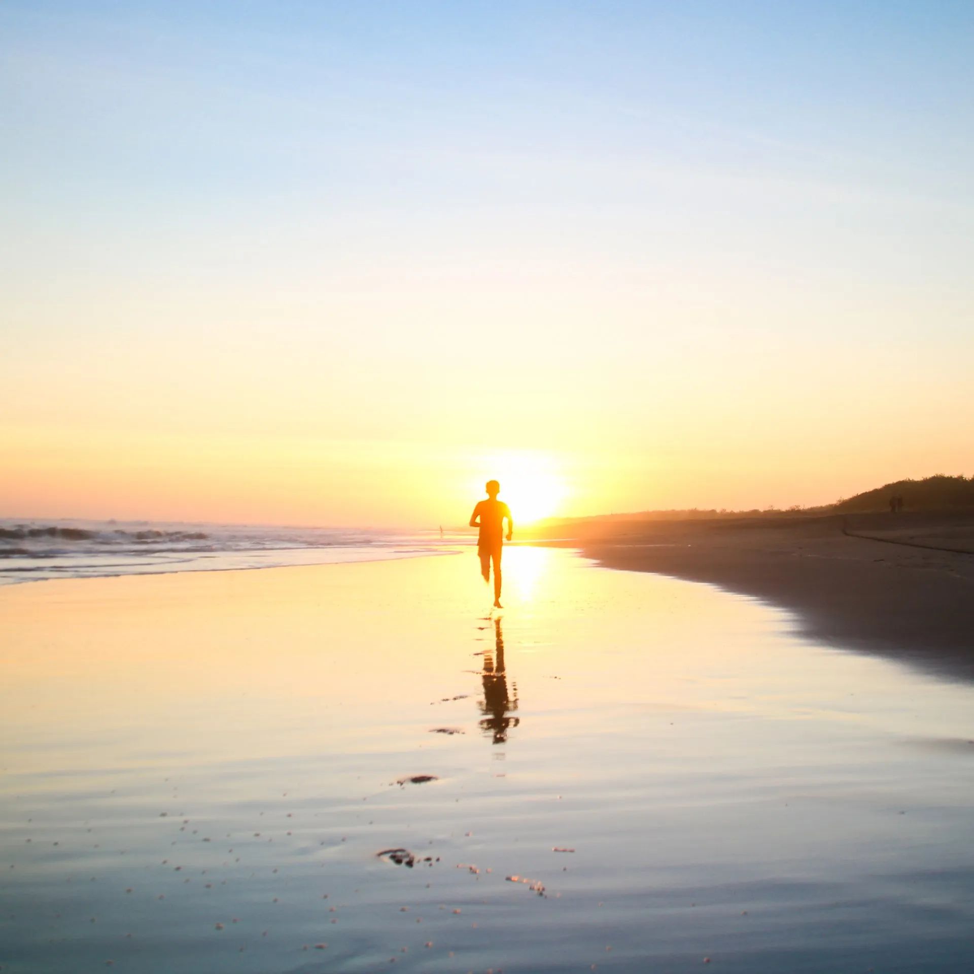 Person running on a beach at sunrise, with golden light reflecting on wet sand.