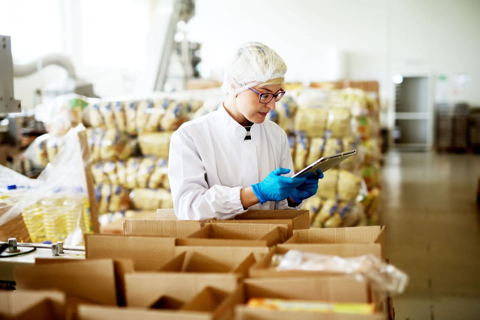 Worker in white uniform and blue gloves inspecting produce in a warehouse with boxes in the foreground
