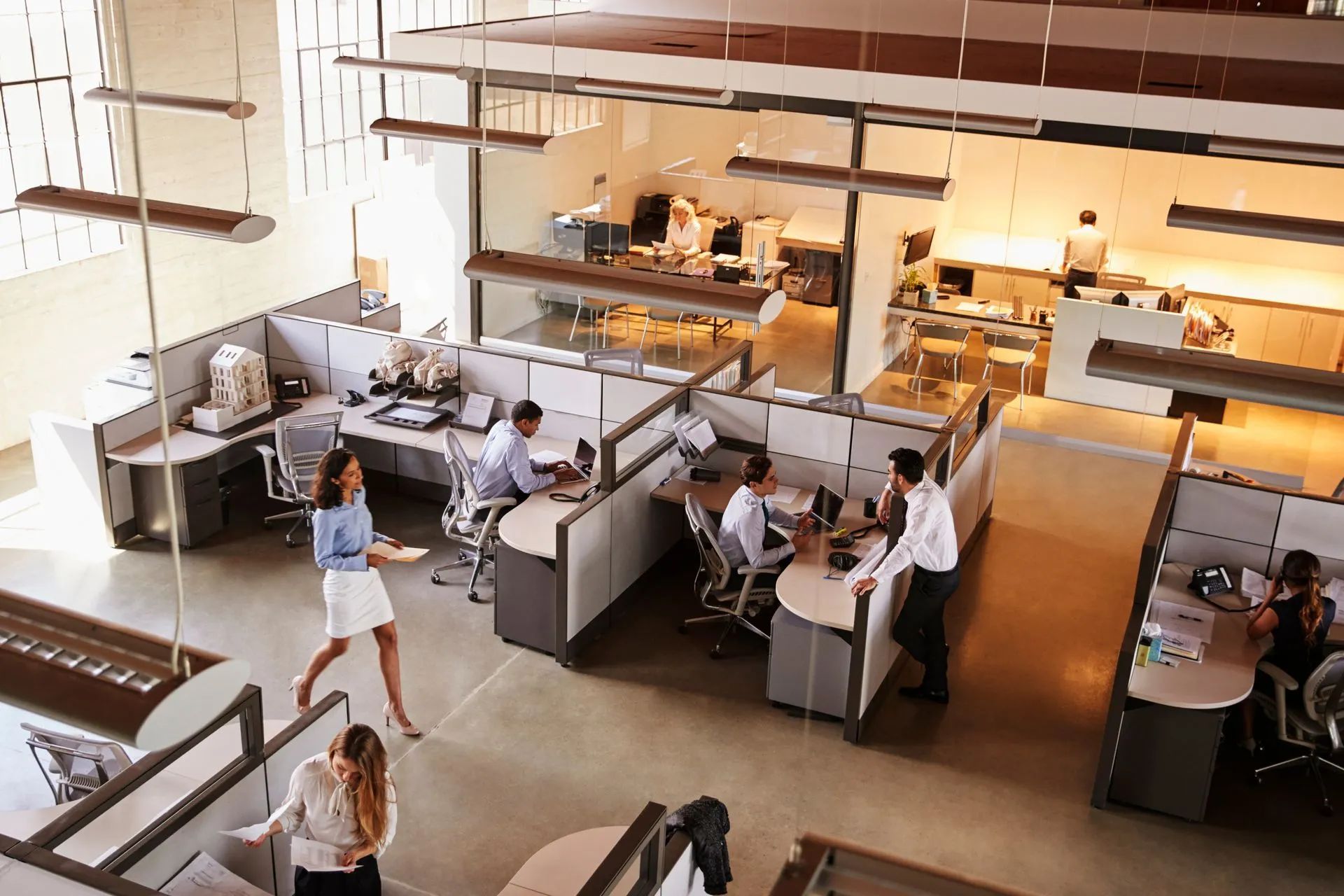 Open-plan office with people working at desks and walking through a bright, modern workspace.