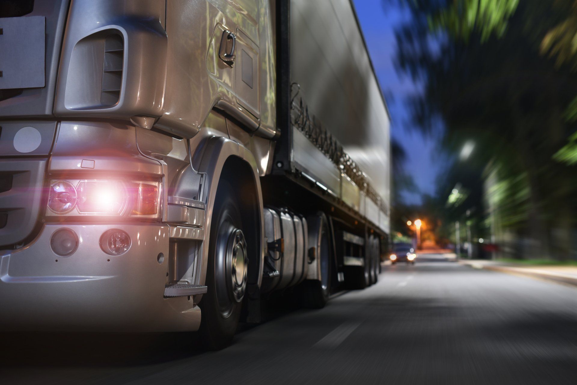 A silver semi-truck speeding on a road at night, with motion blur and taillights glowing.