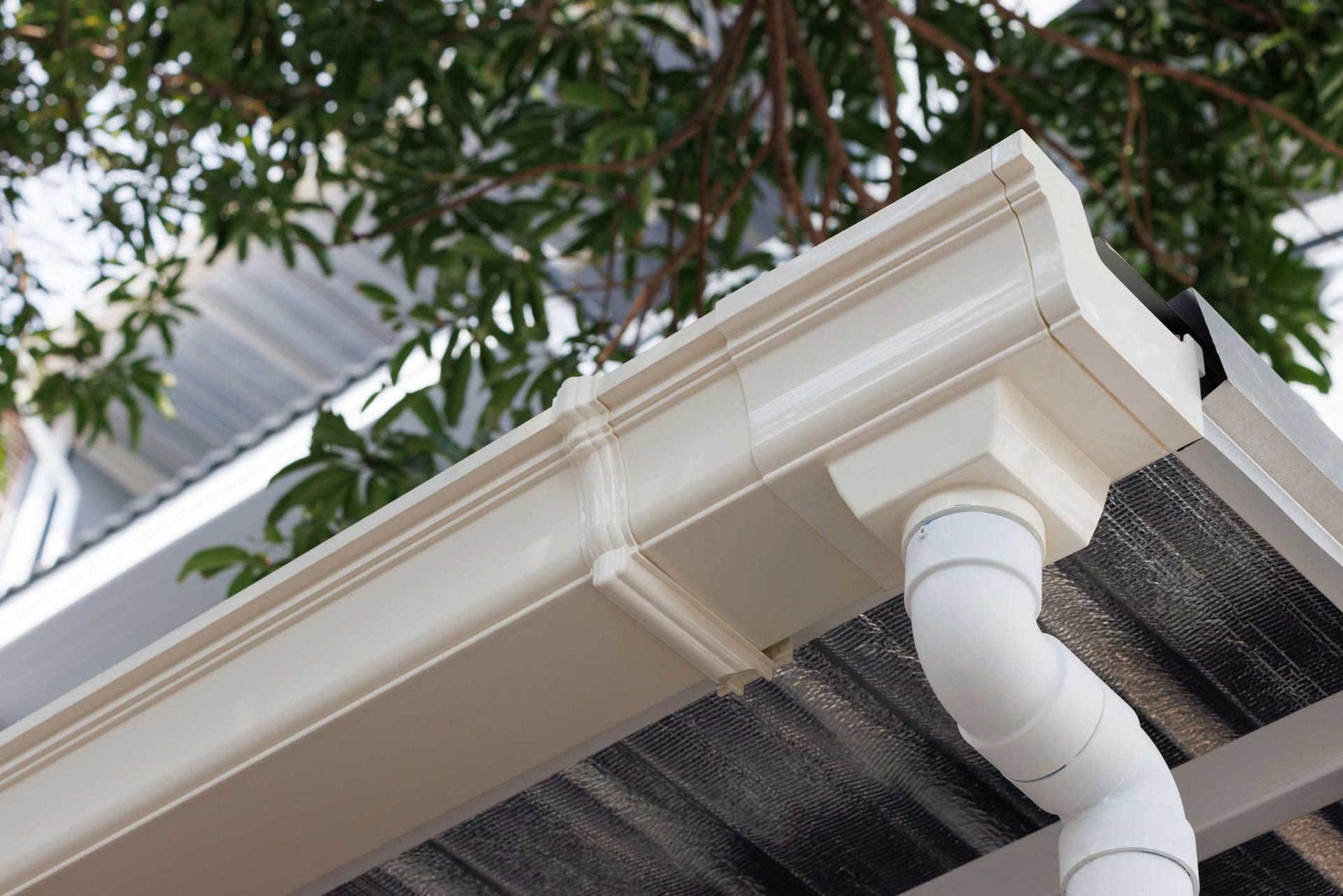 White Plastic Rain Gutter Of Roof Of House. Vinyl Rain Gutter And Downpipe — Moundville, AL — JD Johnson Roofing White Plastic Rain Gutter Of Roof Of House. Vinyl Rain Gutter And Downpipe — Moundville, AL — JD Johnson Roofing