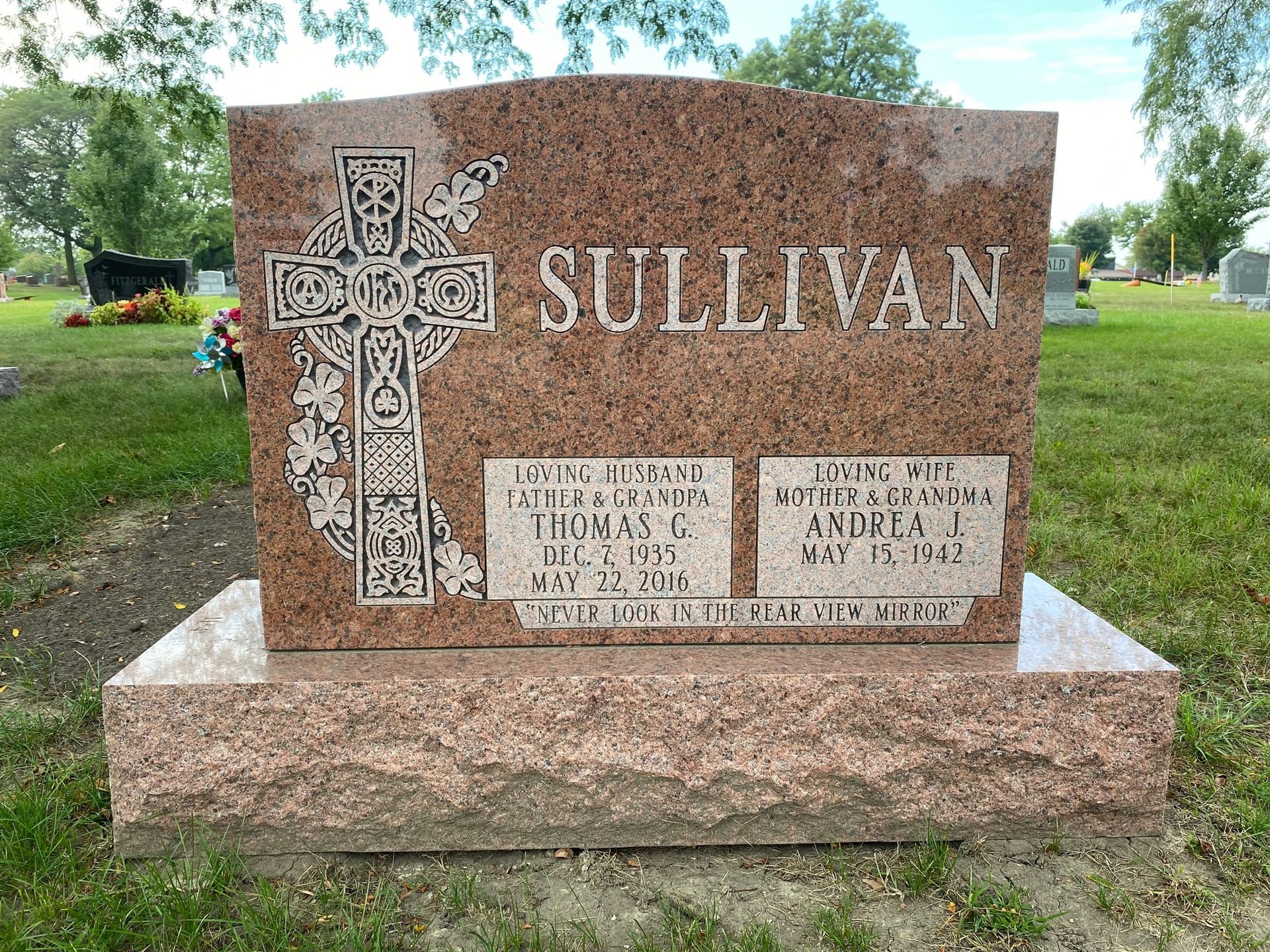 A pink granite Sullivan family headstone in a cemetery, featuring a carved Celtic cross and dates for Thomas and Mary.