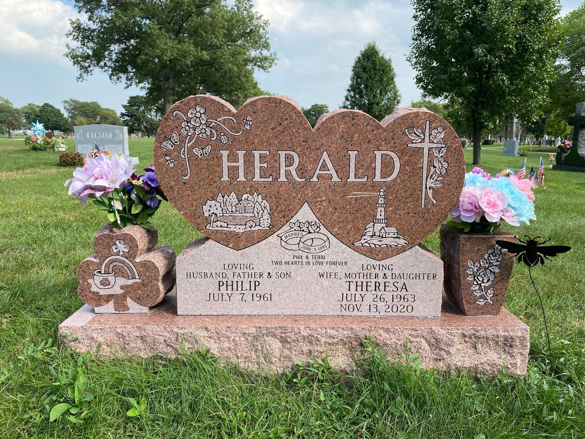 A red granite double-heart gravestone for the Herald family, featuring floral engravings and vases in a cemetery.