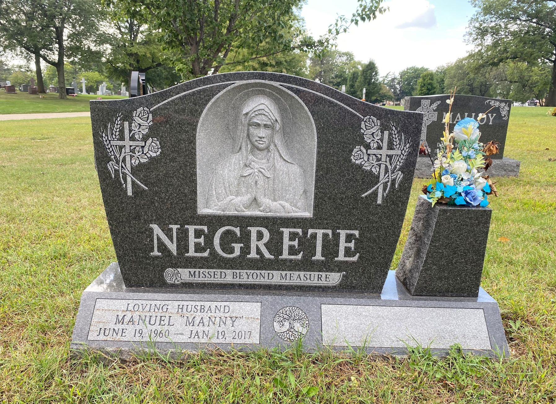 A black granite tombstone for the Negrete family, featuring a carved relief of a figure and floral accents in a cemetery.