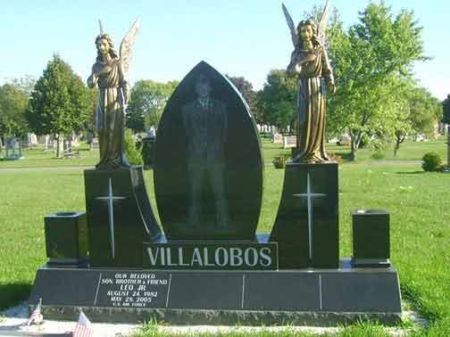 A black granite tombstone for the Villalobos family featuring a portrait, two angel statues, and engraved text in a park.