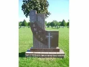 A tan granite tombstone in a grassy cemetery, featuring the vertical name 