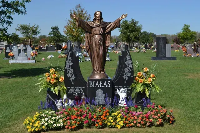 A bronze statue of Jesus with arms outstretched, centered on a black granite monument inscribed 