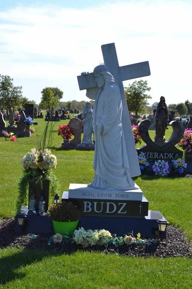 A tombstone with a statue of Jesus carrying a cross, inscribed with the name 