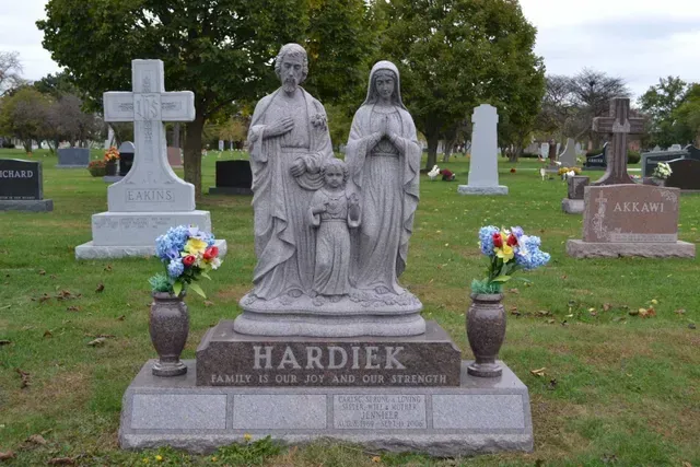 A cemetery headstone featuring a statue of the Holy Family, with 