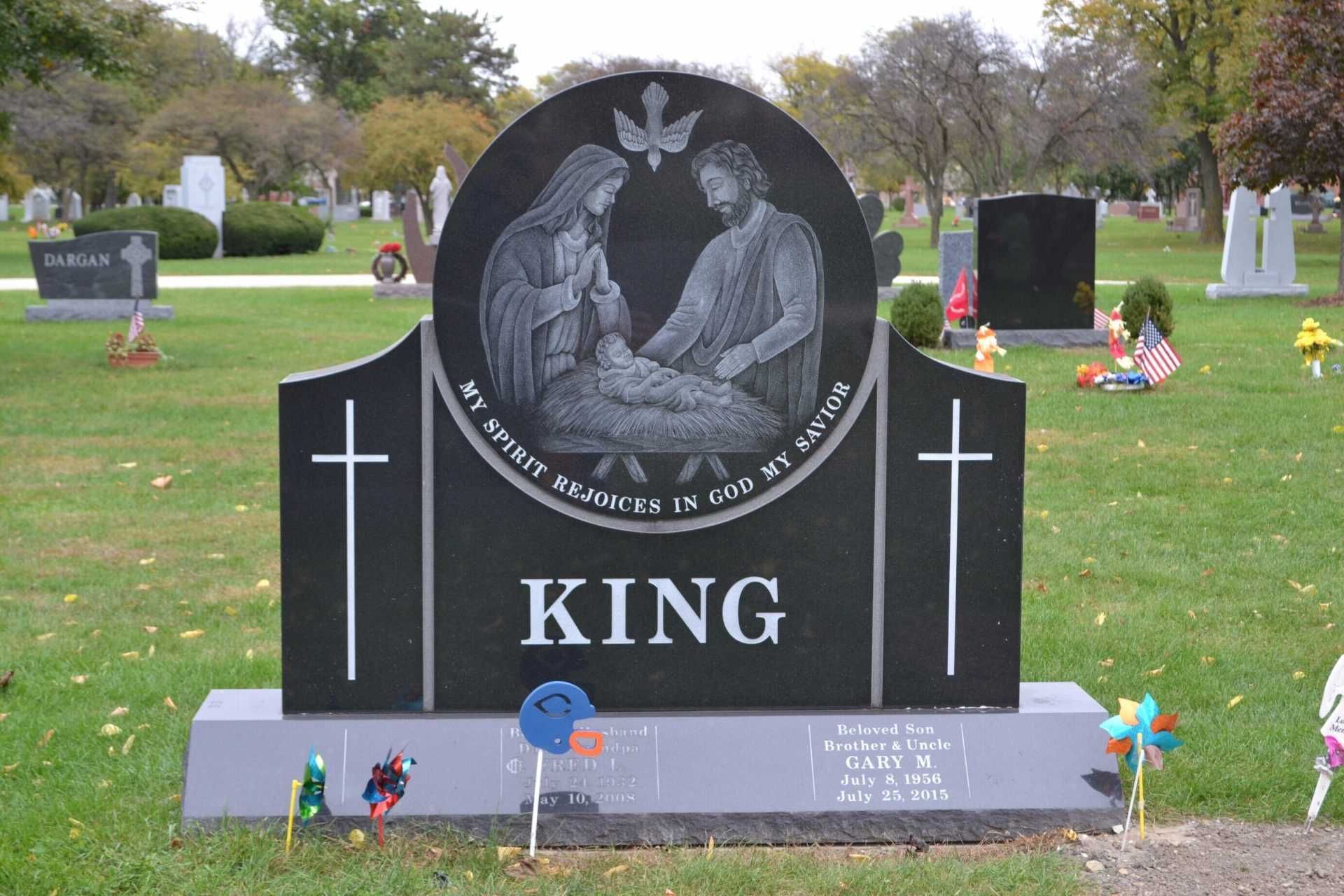 Black granite headstone with family scene and cross, in a cemetery.