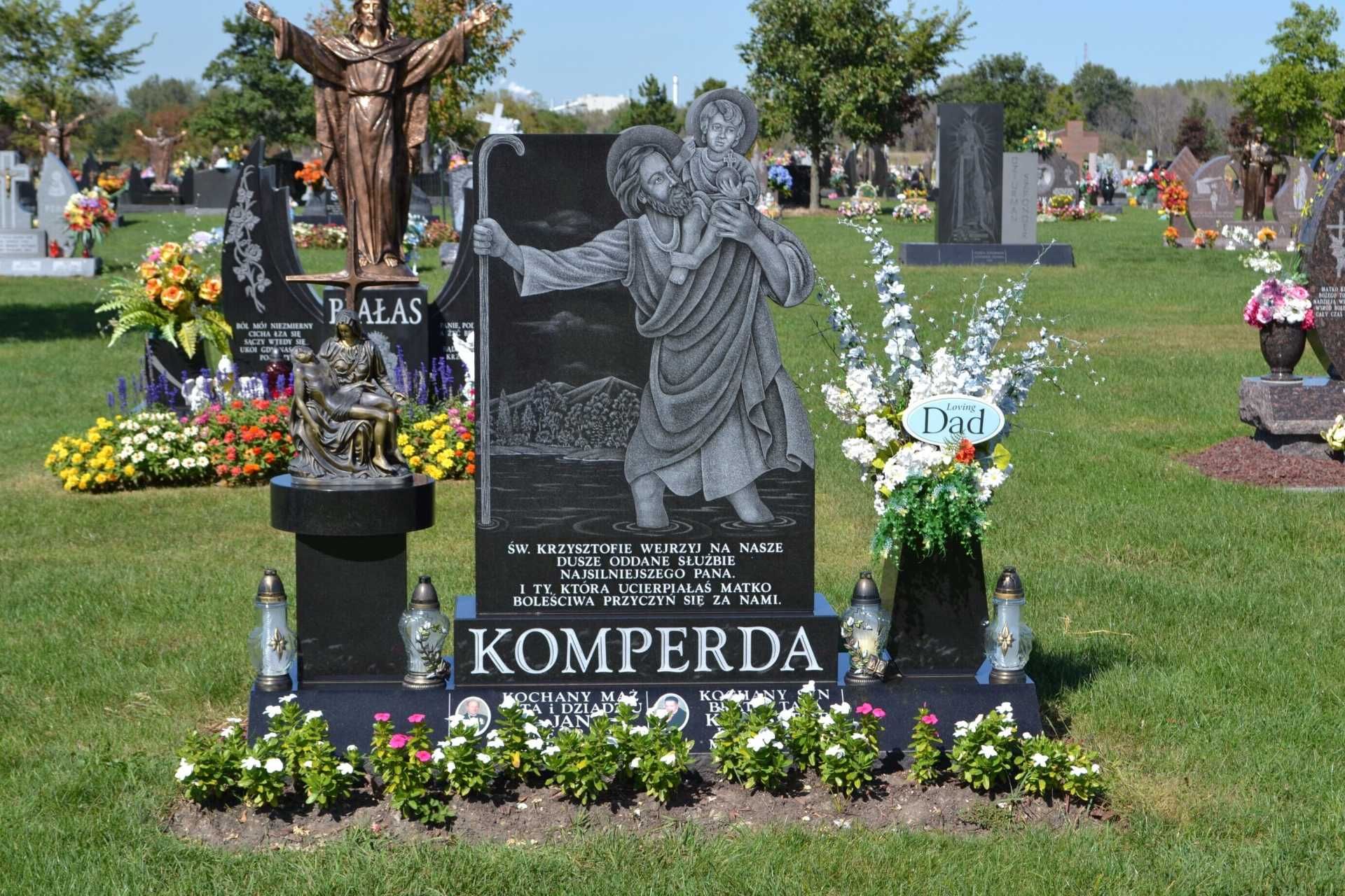Grave at cemetery with engraved image of a saint, flowers, and Komperda name.