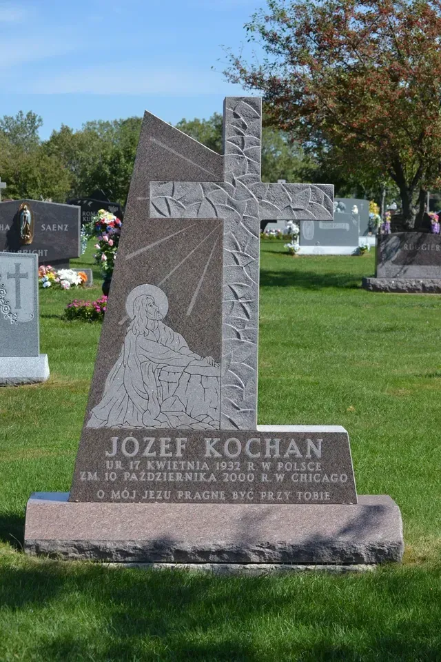 A granite gravestone for Jozef Kochan in a cemetery, featuring a carved cross and a religious figure in a grassy setting.