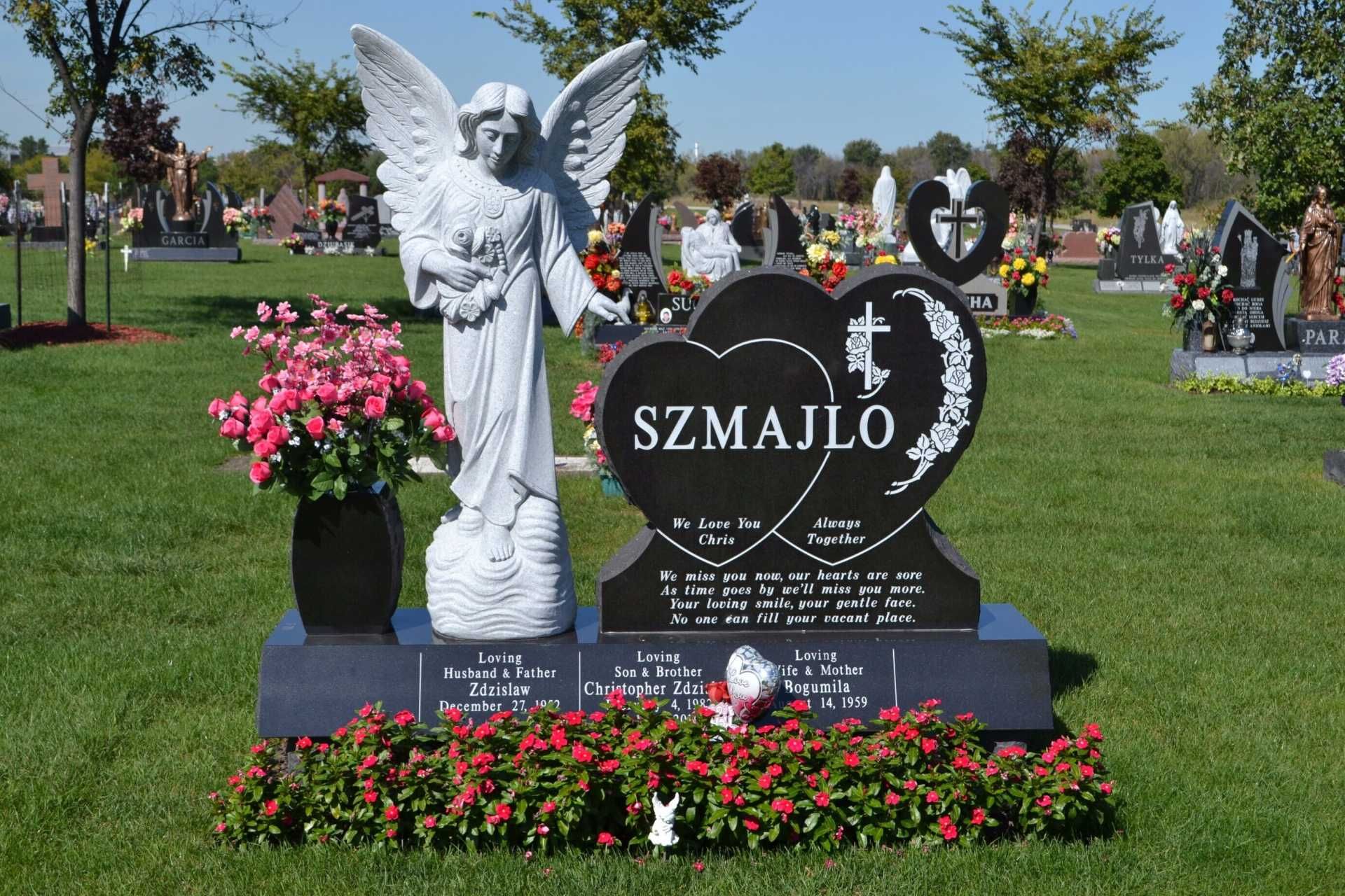 Gravestone with angel statue and flower arrangements in a cemetery.