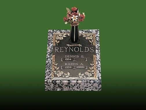 Bronze memorial plaque with flowers atop granite base; reads