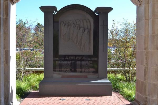 Stone memorial with arched top, carved figures, and inscriptions, viewed through an archway.