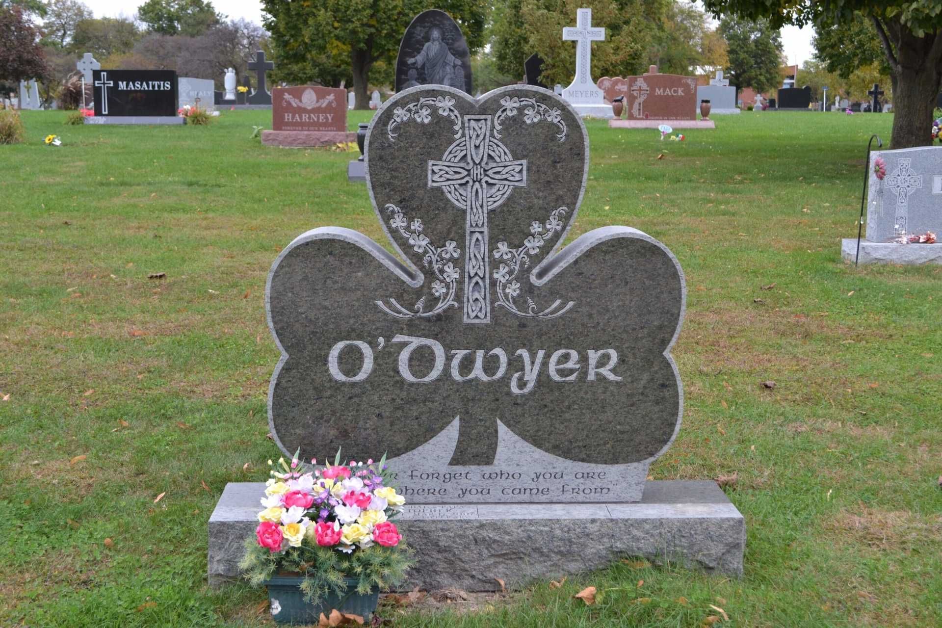 A clover-shaped dark granite headstone engraved with a Celtic cross and the name O'Dwyer, set in a cemetery.