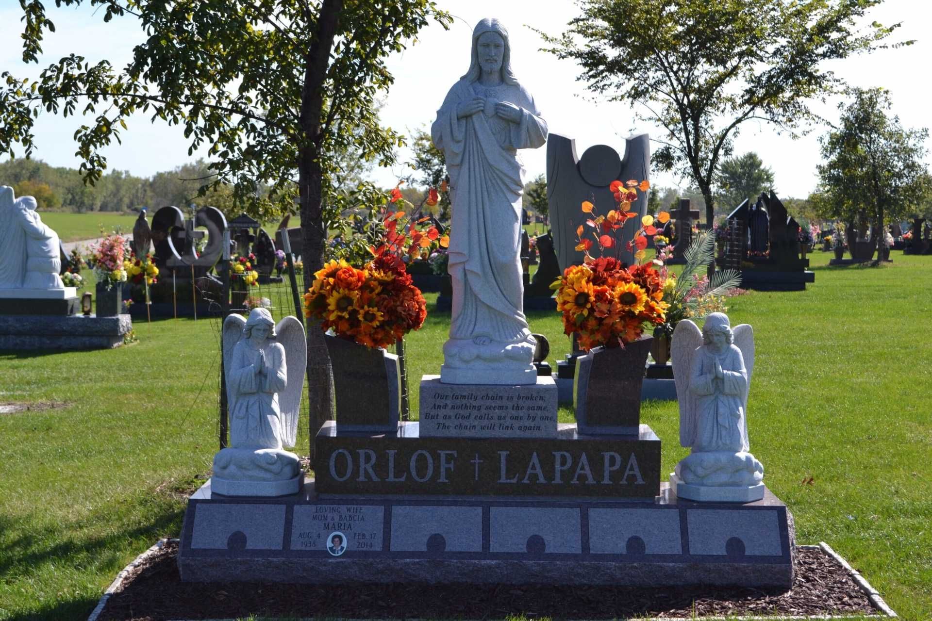 Cemetery gravestone with a white statue, flowers, and two angel statues. 