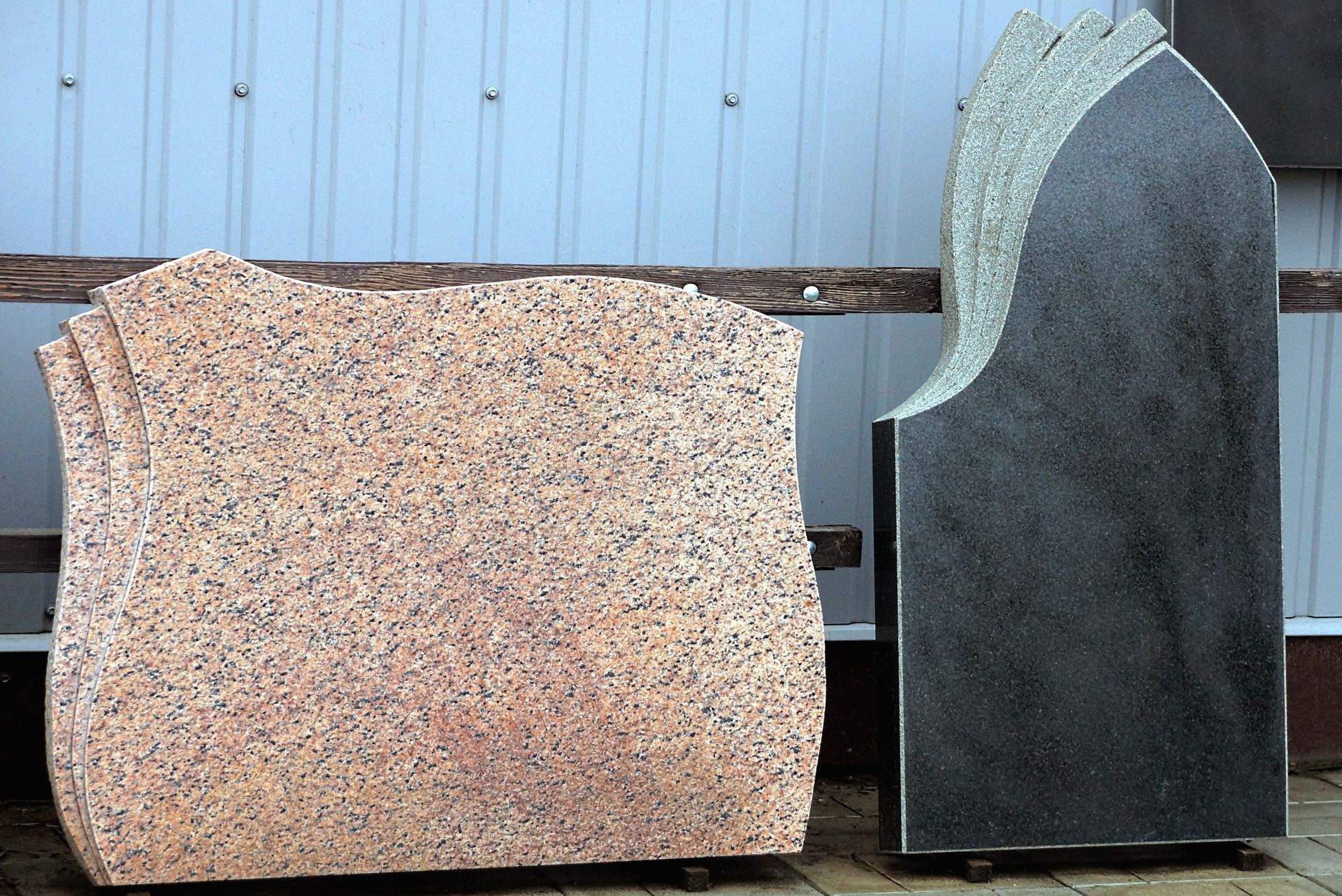 Stacked granite headstones and stone slabs displayed upright against a workshop wall.