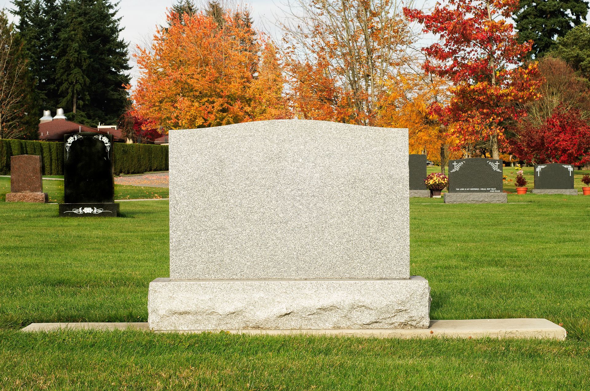 Blank gray granite upright headstone on a grassy lawn with autumn trees in the background