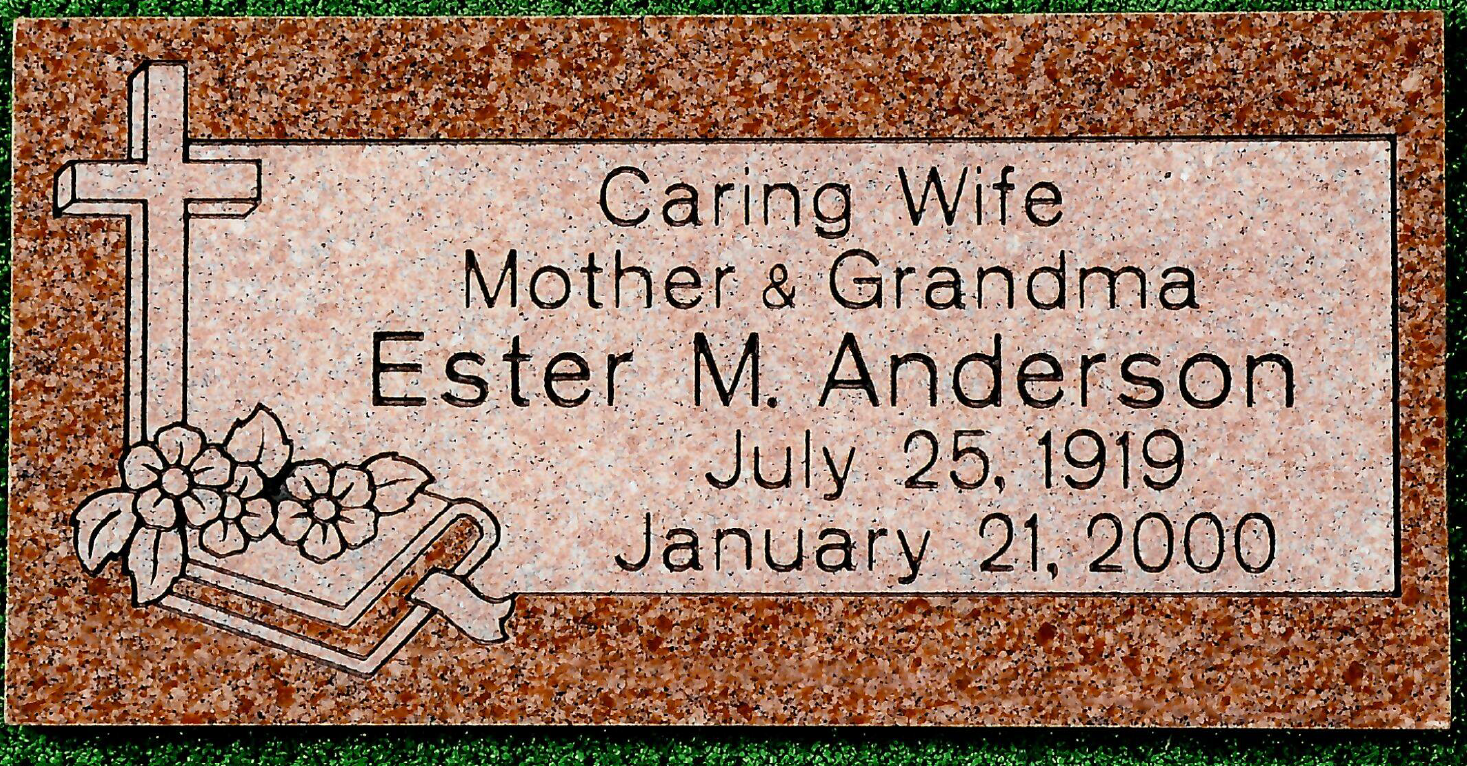 A rectangular red granite headstone with a cross and flowers, inscribed